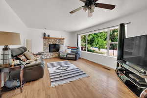 Living area with a ceiling fan, wood finished floors, and a stone fireplace
