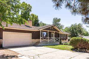 View of front of home with concrete driveway, a chimney, covered porch, an attached garage, and brick siding