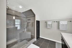 Full bathroom with a textured ceiling, lofted ceiling, a shower stall, vanity, and tile patterned flooring