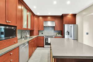 Kitchen featuring appliances with stainless steel finishes, range hood, a kitchen island, light stone counters, and backsplash