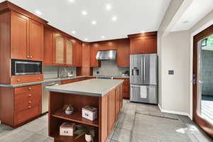 Kitchen featuring stainless steel appliances, tasteful backsplash, under cabinet range hood, light countertops, and glass insert cabinets