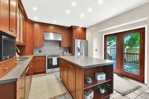 Kitchen with under cabinet range hood, appliances with stainless steel finishes, decorative backsplash, open shelves, and recessed lighting