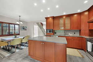 Kitchen featuring a chandelier, stainless steel appliances, a center island, backsplash, and glass insert cabinets