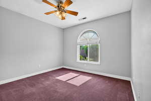 Spare room featuring dark colored carpet and a ceiling fan