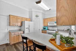 Kitchen with crown molding, white appliances, a peninsula, a breakfast bar area, and light countertops