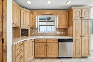 Kitchen with light brown cabinetry, dishwasher, decorative backsplash, light countertops, and a textured ceiling