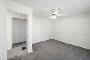 Unfurnished bedroom featuring dark colored carpet, crown molding, and ceiling fan