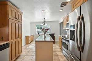 Kitchen with appliances with stainless steel finishes, a kitchen island, a chandelier, ornamental molding, and hanging light fixtures