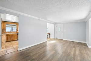 Unfurnished living room with a textured ceiling, light wood-type flooring, and ornamental molding