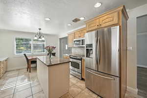 Kitchen with stainless steel appliances, backsplash, a kitchen island, a chandelier, and dark stone counters