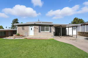 View of front of home featuring a front lawn, an attached carport, concrete driveway, and brick siding
