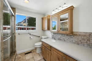 Bathroom featuring a stall shower, vanity, backsplash, and ornamental molding