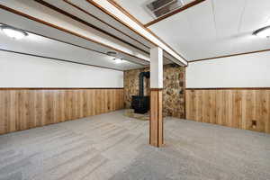 Finished below grade area featuring a wainscoted wall, carpet floors, wooden walls, and a wood stove