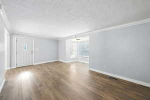Unfurnished living room featuring crown molding, a textured ceiling, and hardwood / wood-style floors