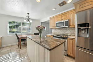 Kitchen featuring stainless steel appliances, backsplash, a chandelier, a kitchen island, and crown molding