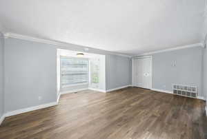 Empty room featuring a textured ceiling, wood finished floors, and crown molding
