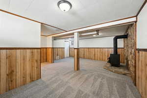 Finished below grade area featuring a wainscoted wall, carpet flooring, wood walls, and a wood stove