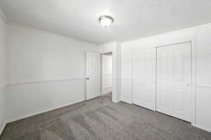 Unfurnished bedroom featuring carpet flooring, crown molding, a closet, and a textured ceiling
