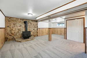 Below grade area featuring wainscoting, a wood stove, carpet flooring, and wooden walls