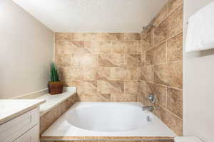 Bathroom featuring a textured ceiling, vanity, and tub / shower combination