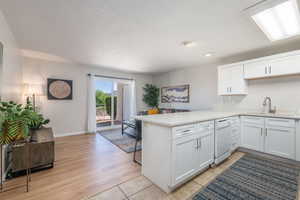 Kitchen featuring a peninsula, light countertops, white cabinetry, a textured ceiling, and white dishwasher