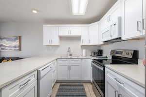 Kitchen with white appliances, white cabinets, light stone counters, light tile patterned flooring, and a peninsula