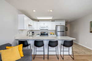 Kitchen featuring a peninsula, stainless steel appliances, light countertops, a kitchen bar, and white cabinetry