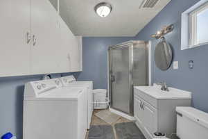 Full bathroom featuring independent washer and dryer, a textured ceiling, a stall shower, and vanity