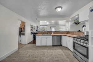 Kitchen with stainless steel appliances, white cabinets, a textured ceiling, and recessed lighting