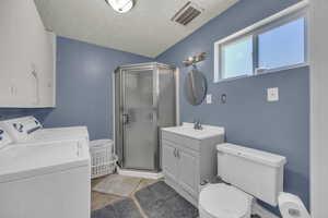 Full bath featuring washer and dryer, a shower stall, two vanities, and a textured ceiling