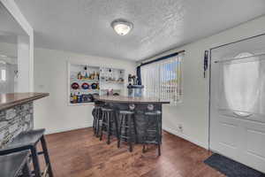 Indoor dry bar featuring dark wood-type flooring and a textured ceiling