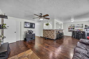 Living room featuring a ceiling fan, hardwood / wood-style flooring, a textured ceiling, and a dry bar