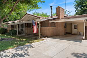 Single story home featuring driveway, brick siding, a carport, and a chimney