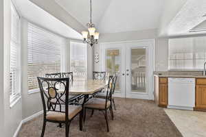 Dining room featuring a chandelier, lofted ceiling, french doors, plenty of natural light, and light colored carpet