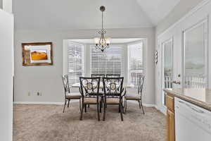 Dining room with light colored carpet, a chandelier, and lofted ceiling