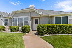 View of exterior entry featuring a yard, stucco siding, a shingled roof, and a chimney