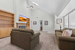Living area featuring carpet flooring, high vaulted ceiling, ceiling fan, a fireplace, and a skylight
