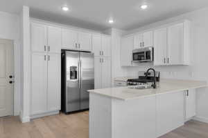 Kitchen featuring appliances with stainless steel finishes, light wood-type flooring, white cabinetry, a peninsula, and recessed lighting