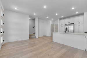Kitchen with white cabinets, light wood finished floors, recessed lighting, light countertops, and stainless steel refrigerator with ice dispenser