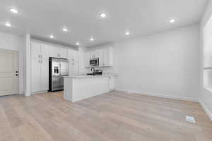 Kitchen featuring a peninsula, stainless steel appliances, white cabinets, light wood finished floors, and recessed lighting