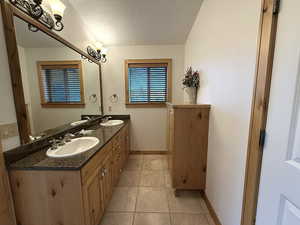 Full bathroom featuring double vanity, tile patterned flooring, and a textured ceiling
