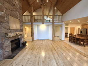 Living area featuring high vaulted ceiling, a stone fireplace, light wood-style flooring, a wood ceiling with exposed beams, and recessed lighting