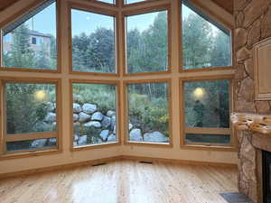 Unfurnished living room featuring wood-type flooring, a high ceiling, a stone fireplace, and healthy amount of natural light