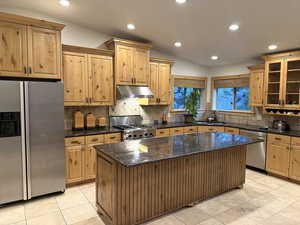 Kitchen with appliances with stainless steel finishes, under cabinet range hood, light tile patterned flooring, tasteful backsplash, and vaulted ceiling