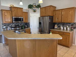 Kitchen with backsplash, light tile patterned flooring, stainless steel appliances, brown cabinetry, and light countertops