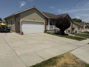 Single story home featuring stucco siding, concrete driveway, a garage, a front lawn, and a porch