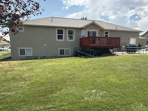 Back of house with a deck, stucco siding, a lawn, and a shingled roof