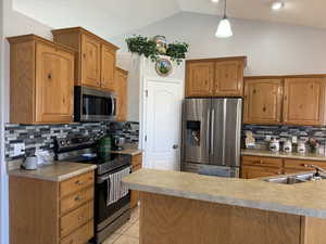 Kitchen with appliances with stainless steel finishes, backsplash, vaulted ceiling, light tile patterned floors, and brown cabinetry