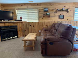 Carpeted living room featuring wood walls and a fireplace