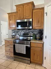 Kitchen with stainless steel appliances, decorative backsplash, brown cabinets, and light tile patterned floors